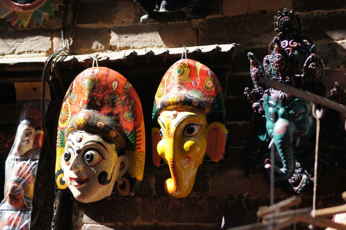 Traditional Newar hand-painted deity masks, including an elephant-headed Ganesha, hanging on a brick wall in Bhaktapur.