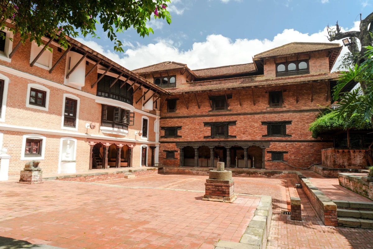 Courtyard in Lalitpur Nepal, featuring traditional Newari brick buildings, carved wooden windows, and a red brick floor.