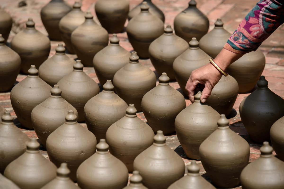 Potter arranging handmade clay pots drying in Pottery Square, Bhaktapur, Nepal.