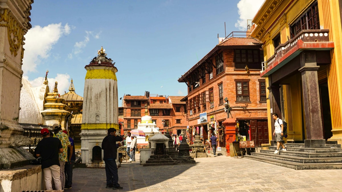 Vibrant Swayambhunath Stupa area filled with ancient shrines, golden roofs, prayer flags, and visitors under a clear sky.