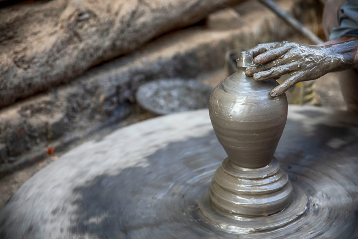 An artisan shapes a clay pot on a pottery wheel in a traditional Nepali workshop.