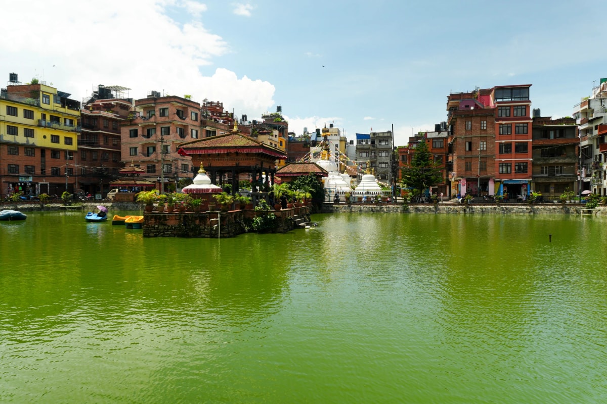 Pimbahal Pond - Patan, Nepal, featuring green water, traditional Newari shrines, and surrounding historic urban architecture.
