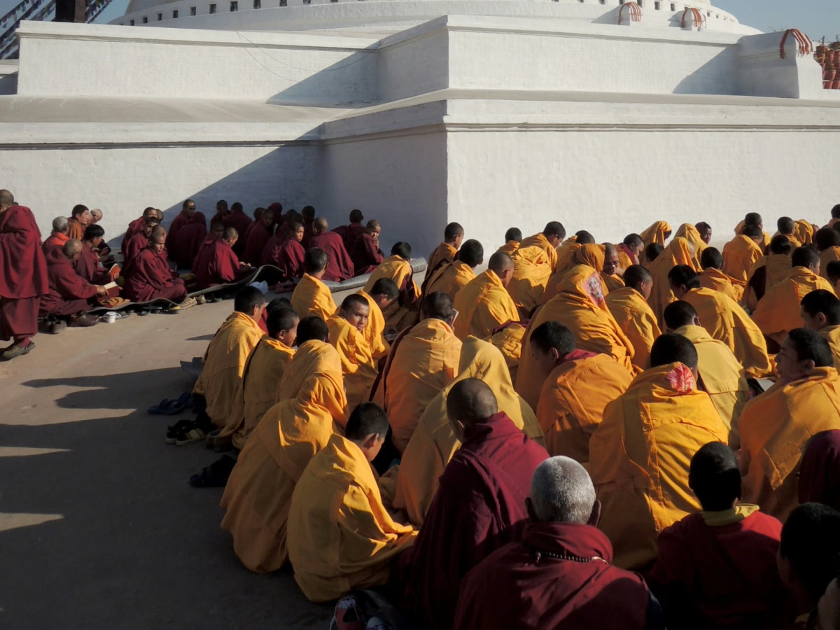 Monks are sitting Infront of the bouddhanath stupa in their yellow robs.